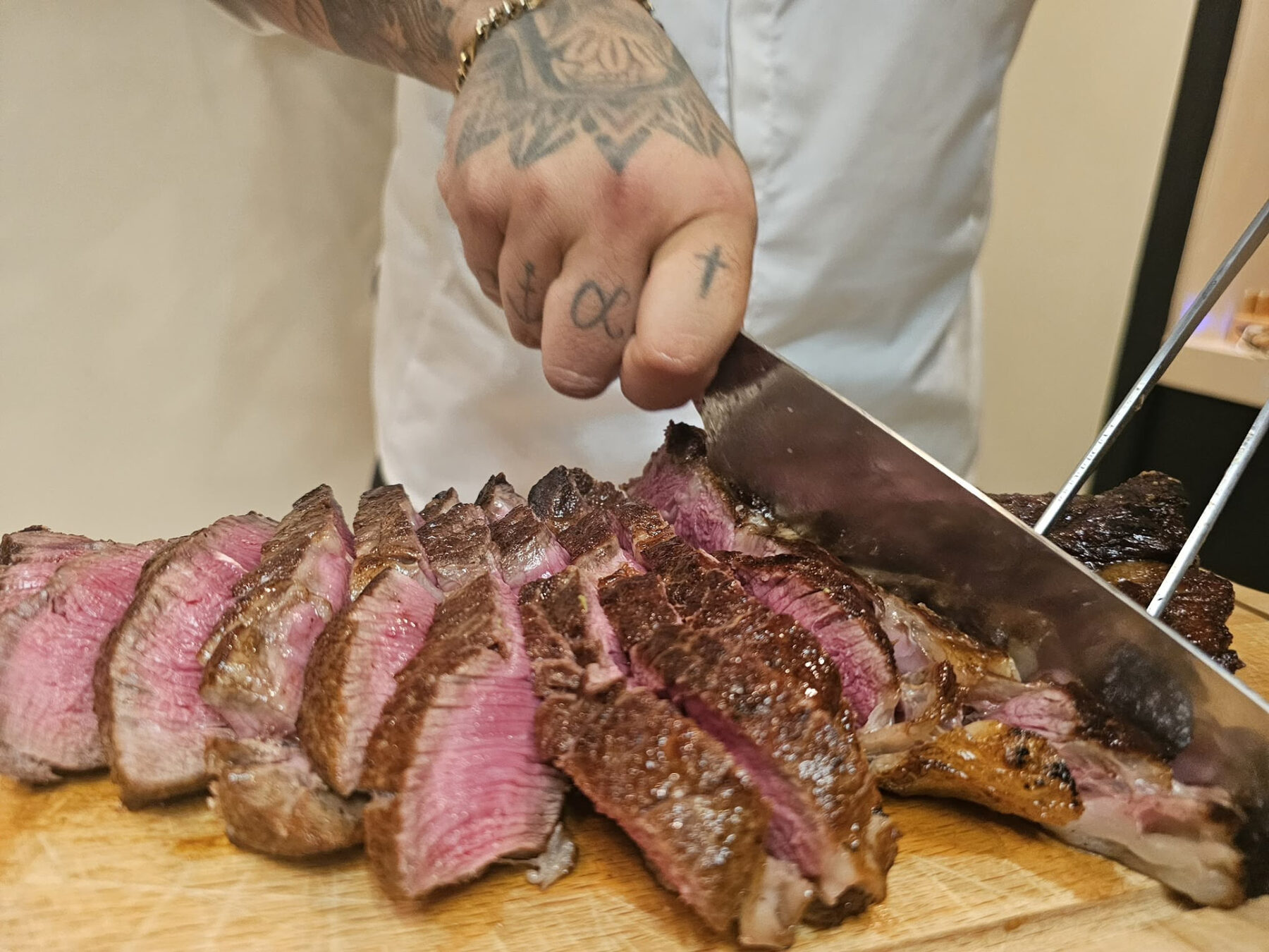 Chef carving a rested cut of beef on a wooden board